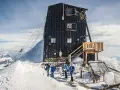 Die Capanna Margherita, eine Berghütte auf einem schneebedeckten Gipfel, mit Bergsteigern, die sich auf den Aufstieg vorbereiten.
