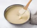 Una spatola di legno mescola una cremosa fonduta di parmigiano in una padella.
