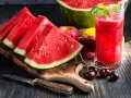 Saftige Wassermelone-Scheiben und ein Glas erfrischender Wassermelonensaft, reich an Vitaminen. Äpfel und Kirschen ergänzen das gesunde Arrangement.