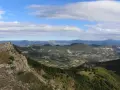 Vue panoramique depuis le col de Perty, avec des montagnes verdoyantes et un ciel bleu parsemé de nuages.