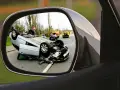 Widok z lusterka: wywrócony samochód, pomarańczowa i żółta ciężarówka na drodze. nnw.