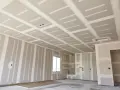 Ściany i sufit z **regipsu** w stanie surowym, z widocznymi połączeniami płyt i przygotowaniem pod instalacje.