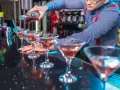 Barman nalewa różowy drink do kieliszków koktajlowych na czarnym blacie.