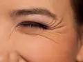 Primer plano de un ojo cerrado con maquillaje, mostrando las arrugas debajo de los ojos que marcan la expresión.