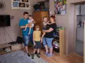 Rodzina z trójką dzieci pozuje do zdjęcia w salonie. W tle widać zdjęcia, telewizor i ozdobne lampki. Ich życie na kredyt nie przeszkadza im w cieszeniu się chwilą.