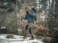Mężczyzna w zimowej kurtce i czapce idzie przez las, używając kijków do nordic walking. Wskazówka, jak dobrać kije do nordic walking, jest kluczowa dla komfortu.
