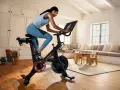A woman rides a Peloton bike, a popular tool for peloton weight loss, in a bright, homey living room.