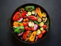 Un assortimento colorato di verdure grigliate, tra cui peperoni, zucchine, pomodorini, cipolle rosse e funghi, disposte in una padella scura.