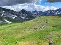 Grupa turystów wędruje po zielonych zboczach gór Macedonii, gdzie w oddali widać ośnieżone szczyty.