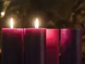 Two lit candles glow on the 2nd Sunday of Advent, their flames casting a warm light on the surrounding purple and pink candles.