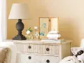 Cómoda de estilo vintage con cajones pintados a la tiza, decorada con lámpara, jarrones con flores y un cuadro de gato.
