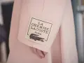 Różowy płaszcz z metką "LA CHEMISE LACOSTE PARIS" z krokodylem, symbol luksusowych marek ubrań.