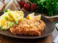 Kotlet schabowy w panierce z ziemniakami i cytryną na brązowym talerzu.