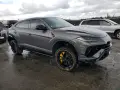 Szary Lamborghini Urus z żółtymi akcentami na felgach, uszkodzony z przodu. Zastanawiasz się nad lamborghini urus cena?