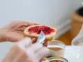 Hände verteilen Marmelade auf Brot. Ein süßer Genuss, der an die besonderen Gelüste in der Schwangerschaft erinnert.