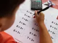 Dziecko zmagające się z zadaniami matematycznymi, być może z dyskalkulią. Widoczne są próby rozwiązań i poprawki.