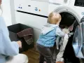 Małe, samodzielne dziecko z ciekawością zagląda do pralki, wyciągając ubrania.