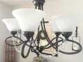 Ciemny metalowy żyrandol z białymi kloszami i kryształkami.