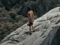 Un homme sur un rocher escarpé, le regard perdu dans le lointain, semble lutter contre sa peur du vide.
