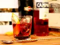 Klasyczny drink z pomarańczą i lodem. Wybór między Negroni czy Boulevardier? Na stole widać butelki Martini, Campari i Jack Daniel's.