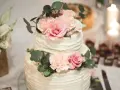 Elegancki tort weselny z kremową dekoracją i pastelowymi kwiatami, ozdobiony gałązkami eukaliptusa.