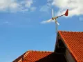 Mała elektrownia przydomowa na tle błękitnego nieba z chmurami. Wirnik turbiny wiatrowej obraca się, dostarczając czystą energię.