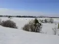 Zimowy krajobraz z zamarzniętym kanałem i zaroślami. W oddali widać pola i drzewa. Śluza Biała Góra w zimowej odsłonie.