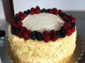Pyszny tort śmietankowo-malinowy z mascarpone, ozdobiony świeżymi malinami i borówkami, posypany złotymi i srebrnymi kuleczkami.