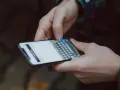 Dłonie trzymają smartfon z klawiaturą. Dowiedz się, jak wydrukować zdjęcie z telefonu, by zachować wspomnienia.