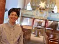 Eine lächelnde evangelische Pfarrerin steht in einer Kirche vor einer Orgel.