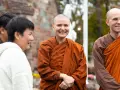 A smiling Buddhist monk in orange robes stands with others outside a church.