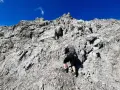 Bergsteigerin klettert über felsiges Gelände, das der UIAA-Skala entspricht. Blauer Himmel und schroffe Felsen.