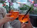 Dwie osoby wznoszą toast Aperolem. Orzeźwiający drink z pomarańczą i truskawką.