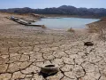Seca tierra agrietada con un lago bajo y barcos varados. Neumáticos abandonados sugieren una contaminación natural y humana.