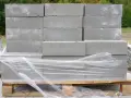 Stos betonowych bloczków fundamentowych na palecie, owiniętych folią.