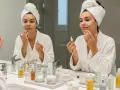Femme appliquant un sérum visage, reflet dans le miroir. Une routine beauté avec des produits de soin, dont un sérum au rétinol pour la peau.