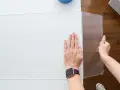 Hands guide a scoring tool along a white acrylic sheet, demonstrating how to cut acrylic sheet for a project.