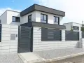 Nowoczesne, biało-szare ogrodzenie z elementami metalowymi i betonowymi, idealnie pasujące do minimalistycznej architektury domu.