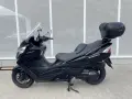 Czarny skuter Suzuki Burgman 400 z kufrem SH46 na tle perforowanej białej ściany.