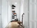 Ein heller, schmaler Flur wirkt optisch breiter durch weiße Türen und eine offene Regalwand mit Schuhen und Accessoires.