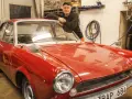 Man lutar sig mot en röd klassisk bil i garage. Lite rost syns på bilens skärmkanter.