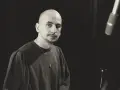 Marek Pędziwiatr, z charakterystyczną łysą głową i wąsikiem, w ciemnej bluzie i z naszyjnikiem, przygotowuje się do nagrania.