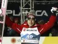 Skoczek narciarski w czerwonej kurtce i czapce z polską flagą świętuje zwycięstwo na skoczni. Mistrzostwa świata w skokach narciarskich.