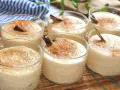 Seis vasitos de cremoso arroz con leche, espolvoreados con canela y decorados con una ramita de canela.