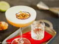 Orzeźwiający drink z martini, ozdobiony połówką marakui, obok kieliszka z wodą i połówki limonki.