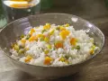 Un tazón de arroz blanco con trozos de zanahoria, guisantes y maíz. Un plato sencillo y colorido de arroz con verduras.