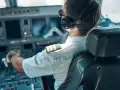 Pilot w słuchawkach i okularach siedzi w kokpicie samolotu, trzymając ręce na sterach.