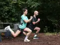 Un couple fait des exercices de renfo course à pied en extérieur, avec des fentes et des squats.
