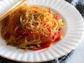 Un piatto di spaghetti di soia con verdure colorate, peperoni rossi, zucchine e carote, guarnito con semi di sesamo.