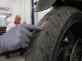 Mano guantata indica il battistrada minimo di una moto, mostrando l'usura.
